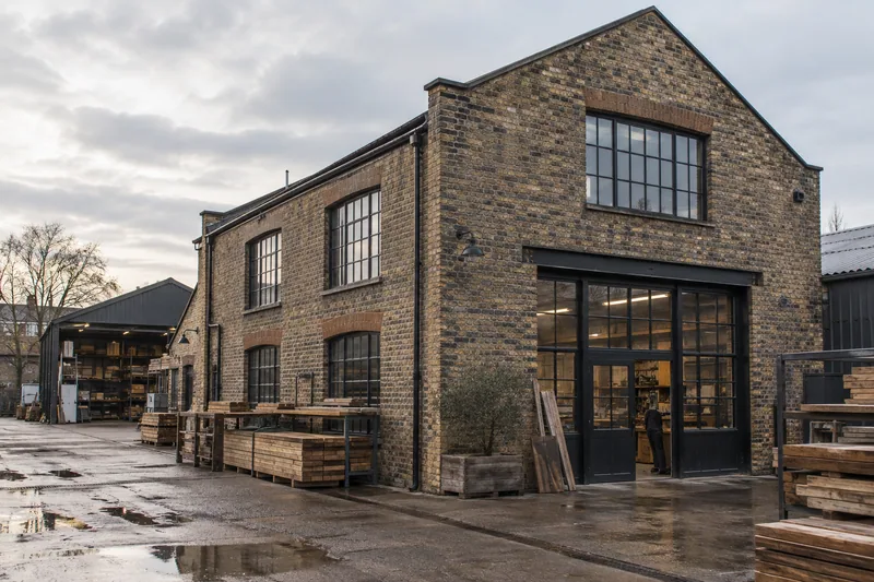 Illustration: Brick construction workshop and yard with stacked timber and steel-framed windows